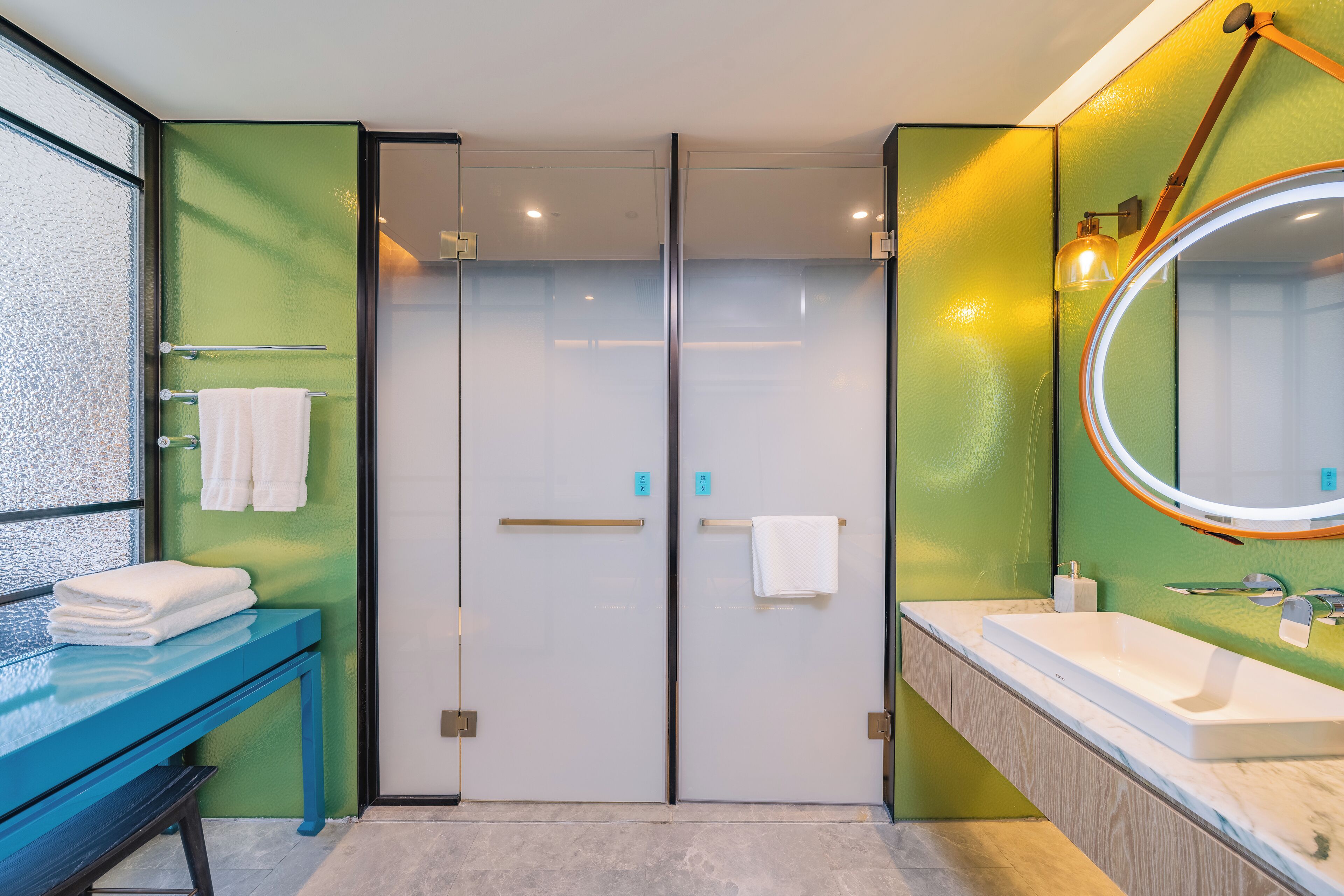 Un baño moderno con cabina de ducha de vidrio, tocador azul y un espejo grande.