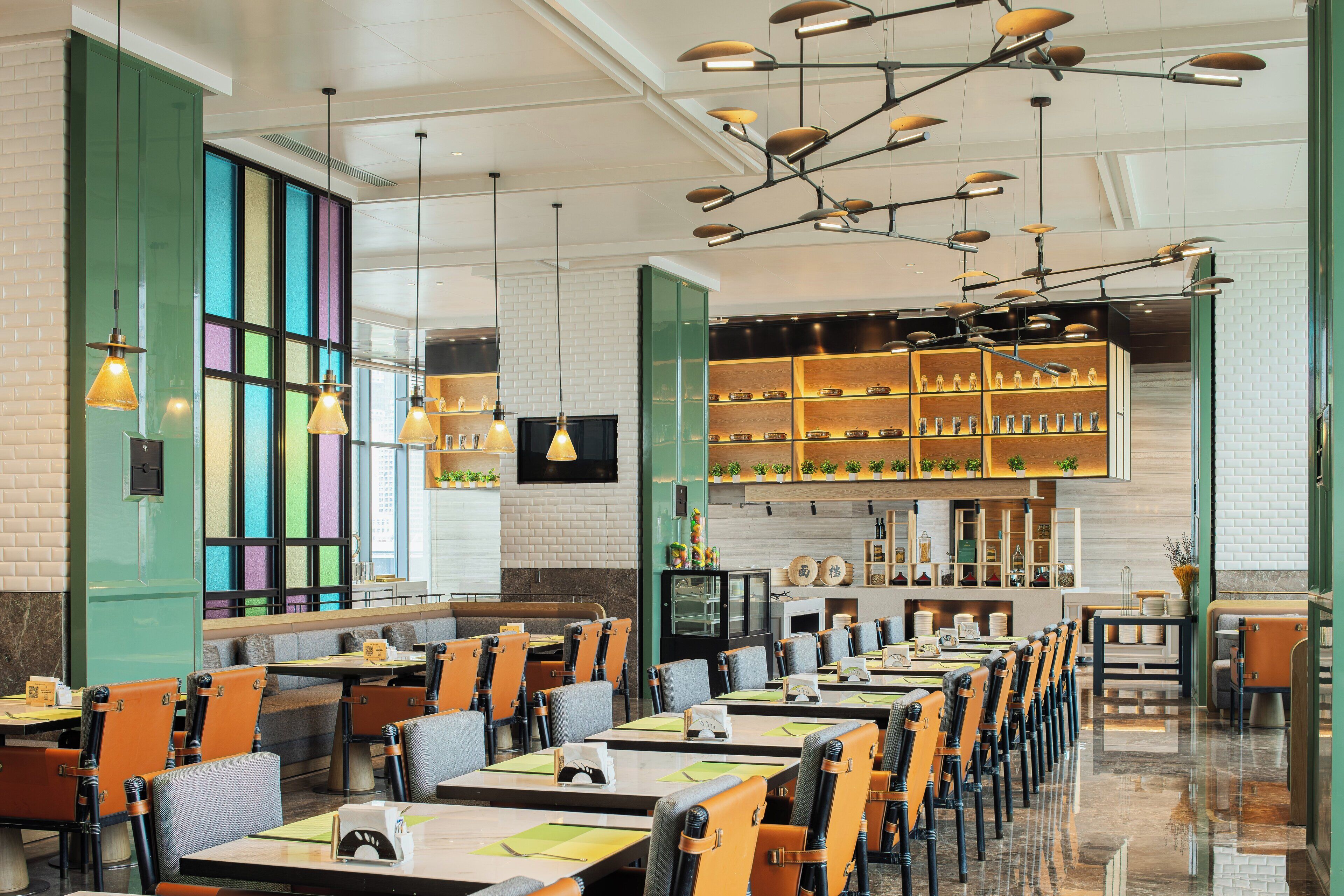 Een modern restaurant met een lange balie, meerdere tafels en stoelen. Er zijn hangende吊灯 en een televisie aan de muur bevestigd.