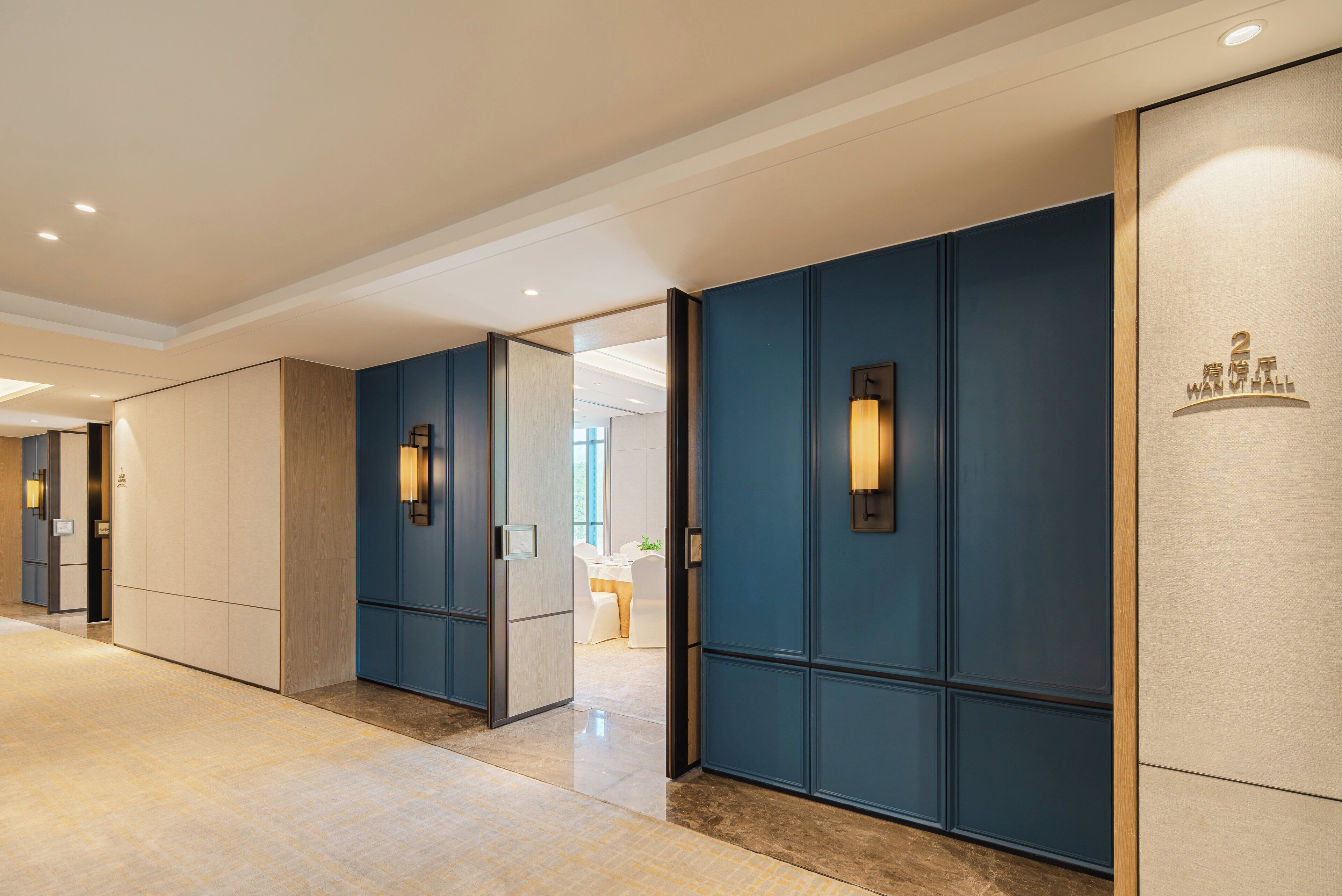 A hotel corridor with blue doors, recessed lighting, and a polished floor.
