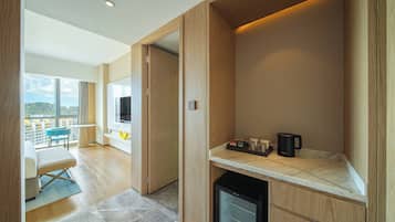A modern hotel room with a balcony, a compact kitchenette, and a large TV.