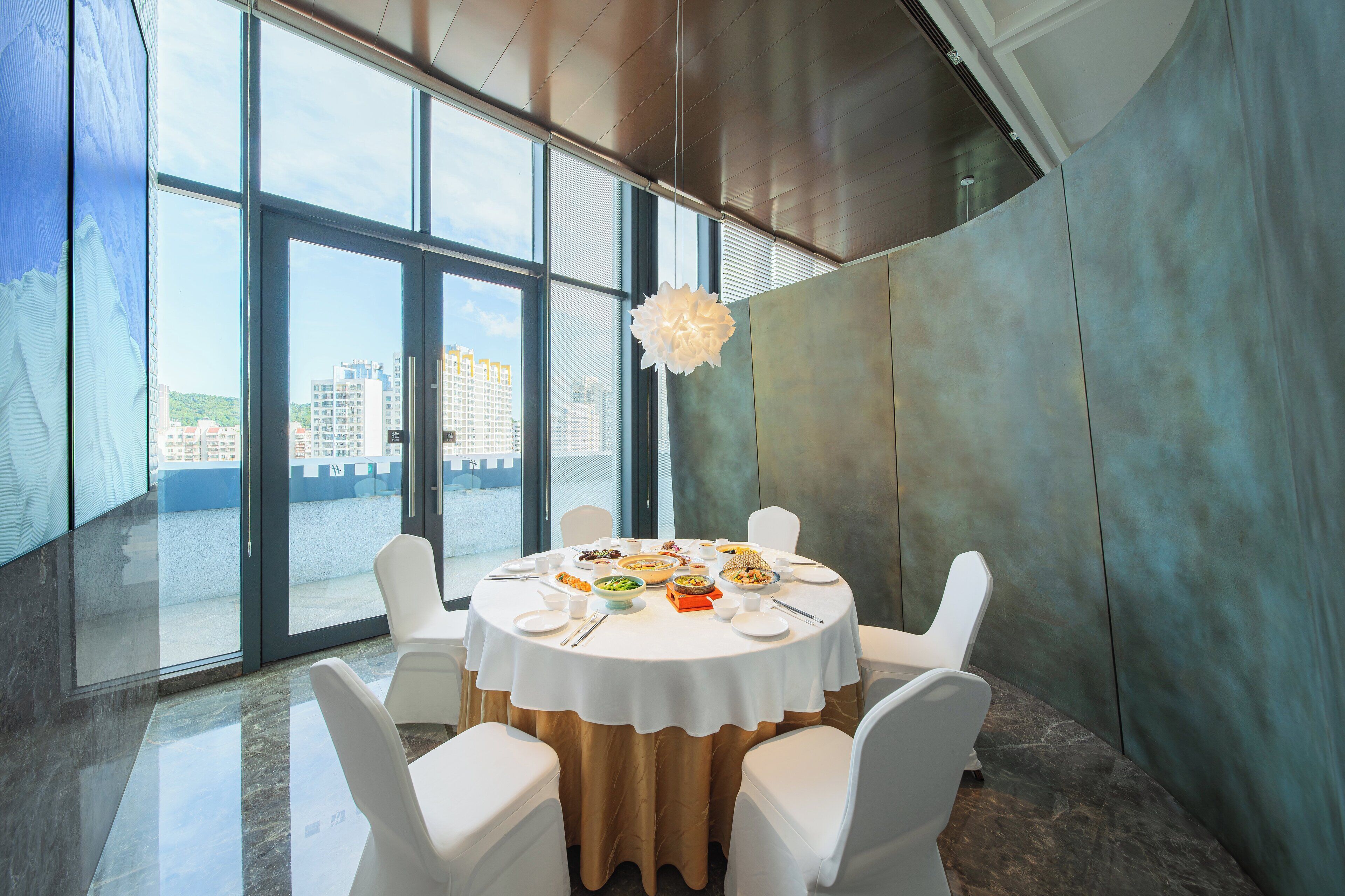 Comedor con una mesa redonda para seis personas, ventanas amplias y vistas a edificios.