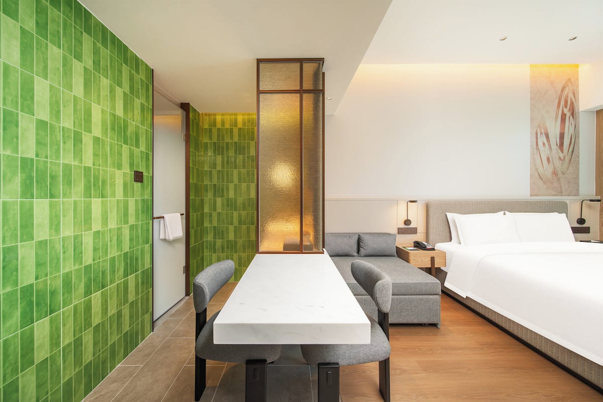 Moderni hotellihuone, jossa on suuri sänky, sohva, ruokapöytä ja vihreillä laatoilla päällystetty seinä.