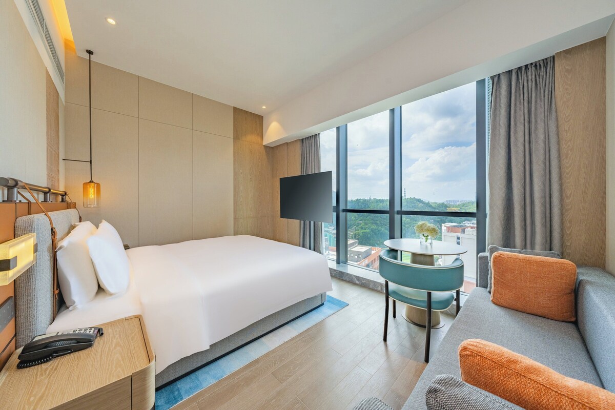 Een hotelkamer met een groot bed, een televisie, een bank en uitzicht op de stad.