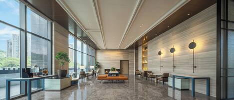 A spacious lobby with large windows, a reception desk, seating area, and modern lighting fixtures.