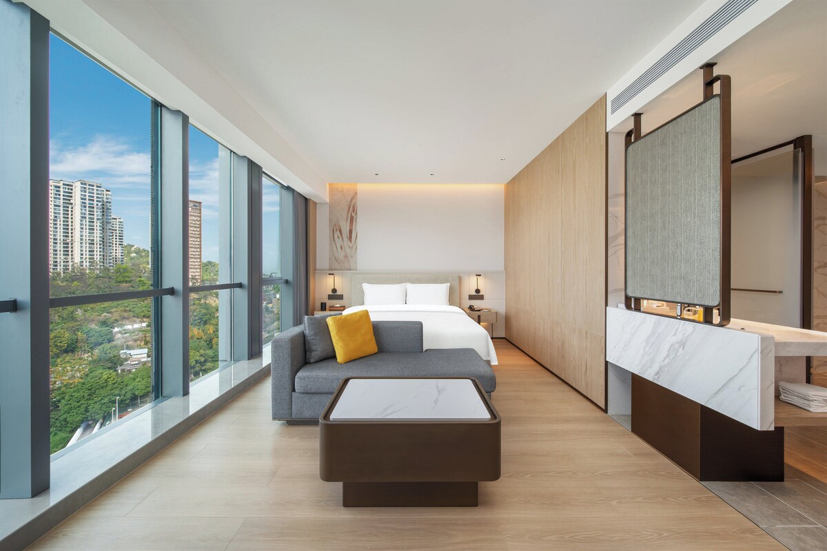 A modern hotel room with a large bed, a sofa, a coffee table, and a bathroom with a mirror.