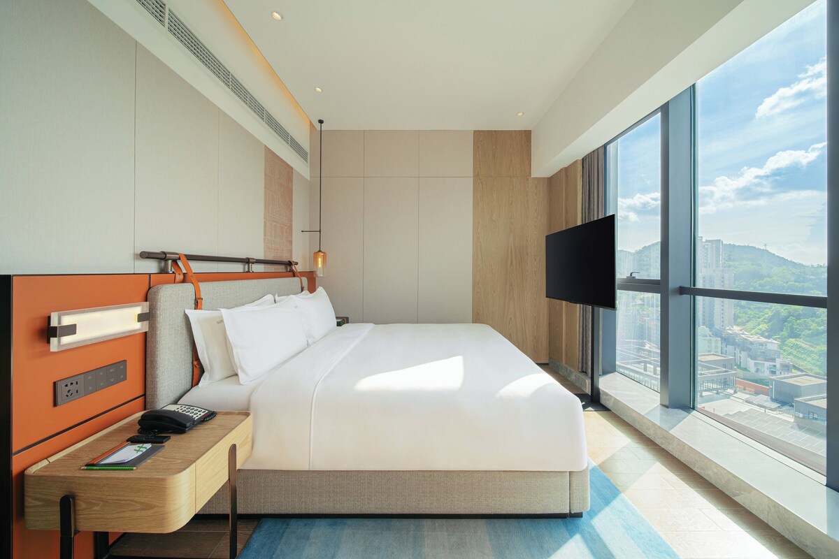 A modern hotel room with a large bed, a desk with a telephone, and a TV.