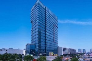 Un edificio de gran altura con fachada moderna de vidrio, rodeado de otros edificios y un cielo despejado.