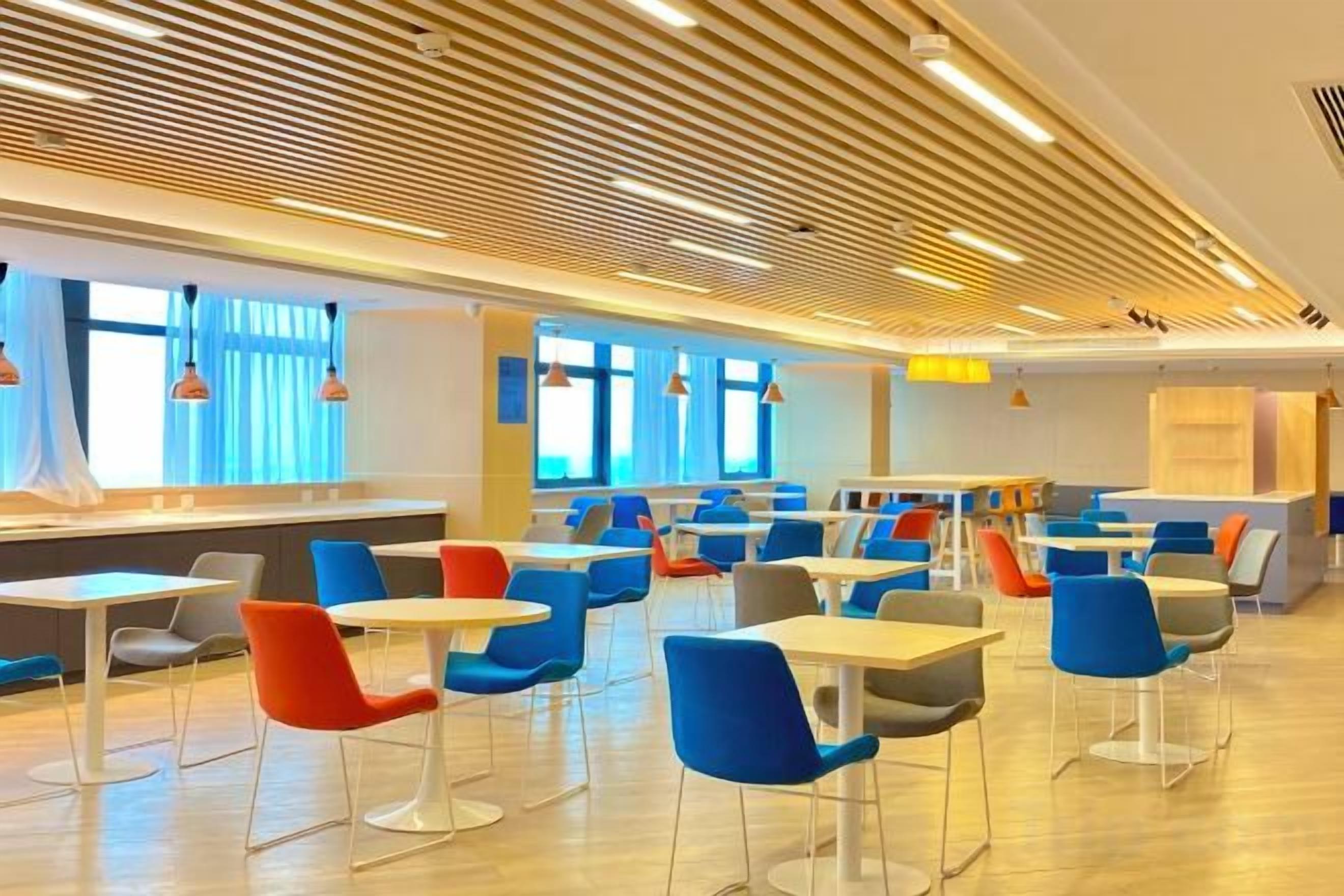 A modern dining area with multiple tables and chairs, large windows, and a wooden ceiling design.