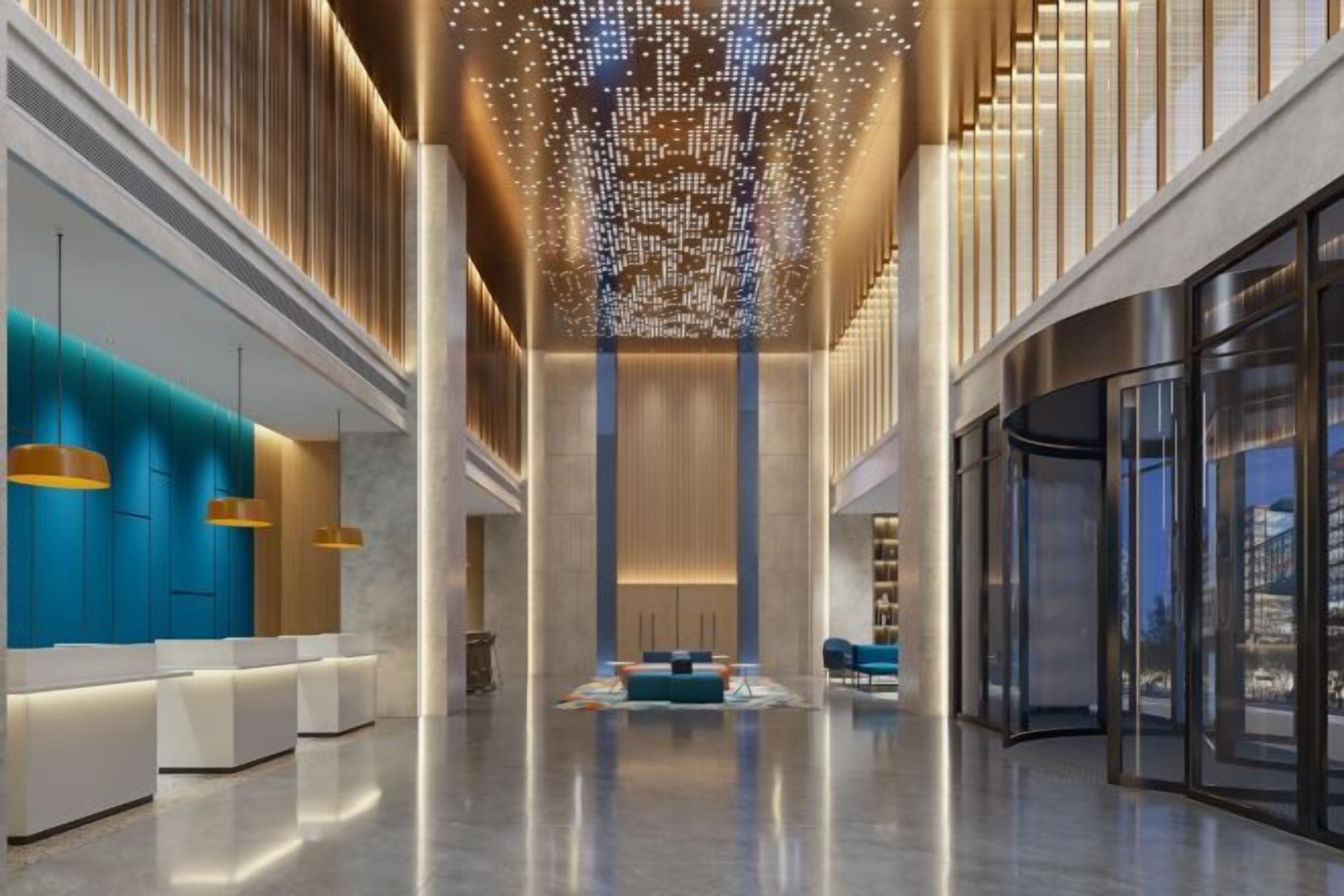 A spacious lobby with a central seating area, a high ceiling with a decorative light fixture, and a glass wall on one side.