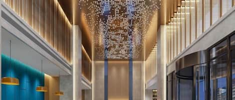 A spacious lobby with a central seating area, a high ceiling with a decorative light fixture, and a glass wall on one side.
