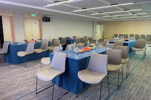 Un salón de conferencias con mesas, sillas, botellas de agua y una pantalla de proyector.