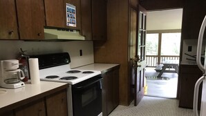 A kitchen with wooden cabinets, a stove, a coffee maker, and a view of a deck with picnic tables.