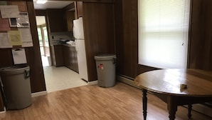 A kitchen with wooden cabinets, a refrigerator, two trash bins, and a window with blinds.