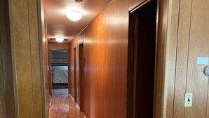A long, narrow hallway with wooden paneling and a wooden floor. There are doors on the right side and a light fixture on the ceiling.