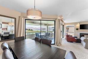 A spacious living area with a large dining table, comfortable seating, a fireplace, and a balcony with a scenic view. - Heavenly Halmalka on Lake Chelan! Comfortably sleeps 8. (Halmalka - Manson)