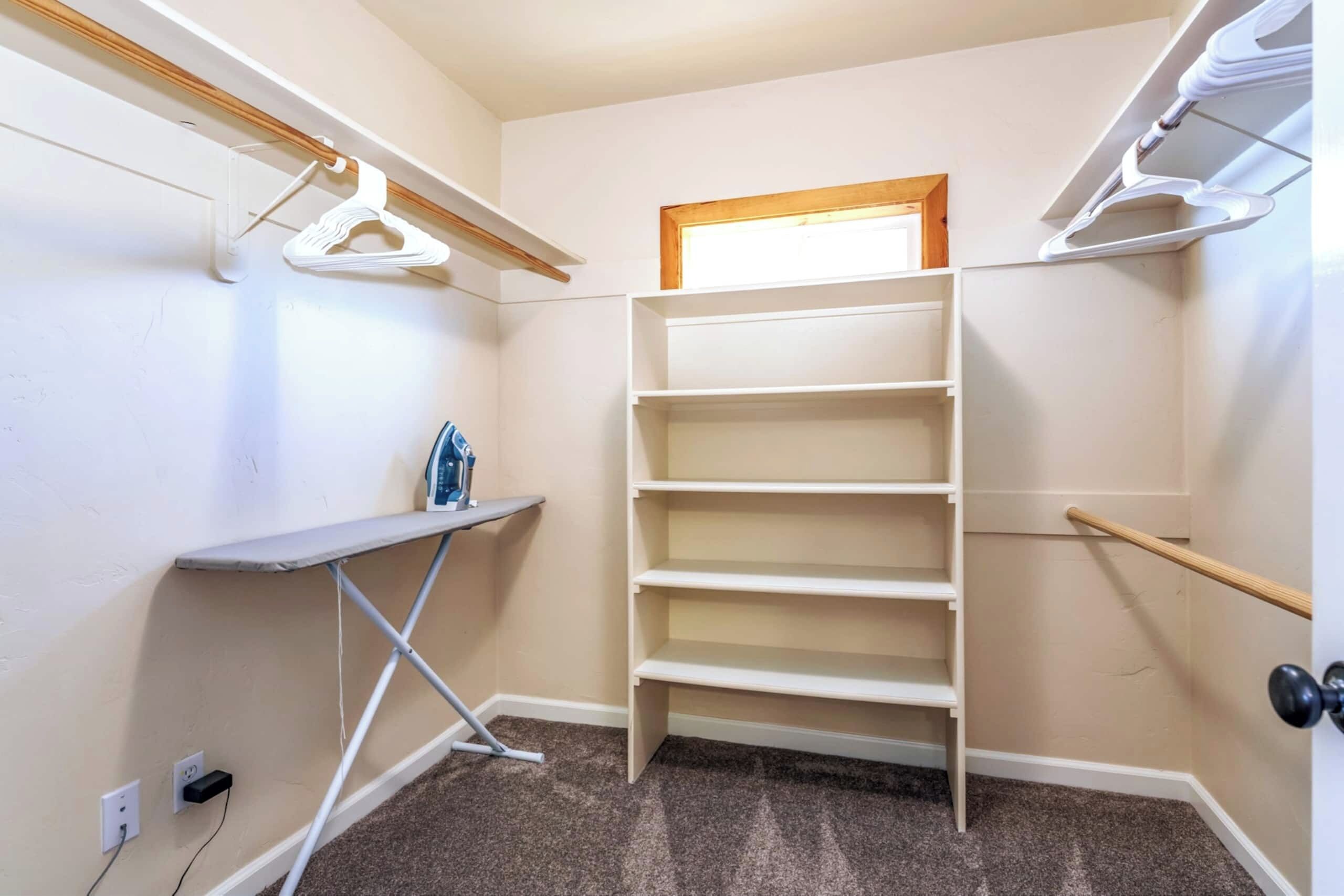 A walk-in closet with a built-in shelf unit, a hanging rack, and a small ironing station.