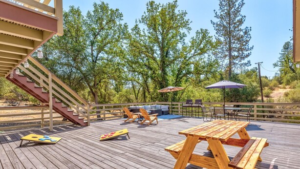 A wooden deck with a picnic table and lounge chairs, surrounded by trees. - 🛶 Cozy Creek Cabin near Yosemite & Bass Lake (Ahwahnee)
