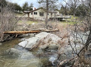 A house with a wooden deck and a stream in front.