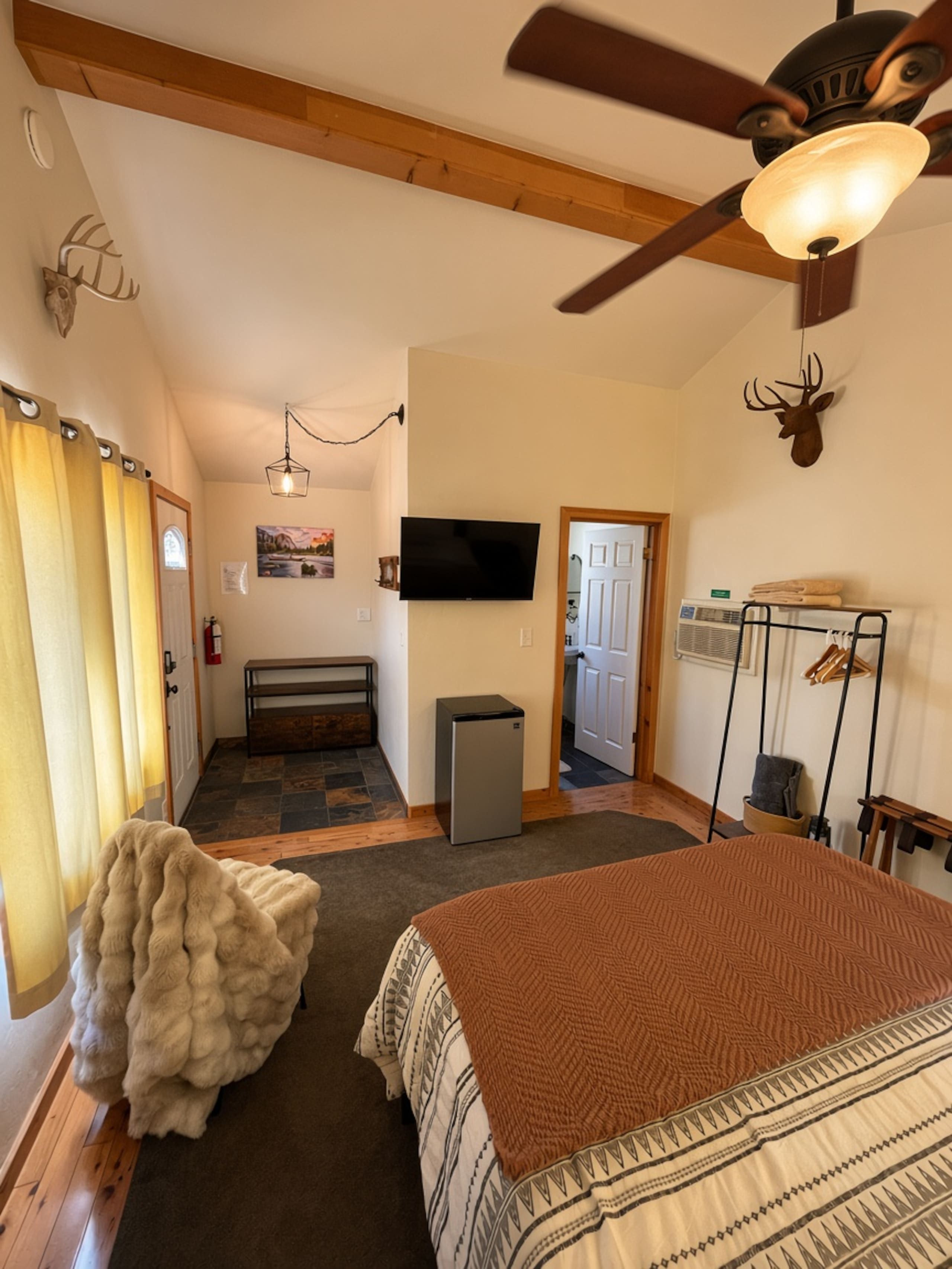 A bedroom with a bed, a ceiling fan, a television, and a fireplace.