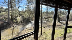 A room with large windows offering a view of a natural landscape with trees and a stream. - 🛶 Cozy Creek Cabin near Yosemite & Bass Lake (Ahwahnee)
