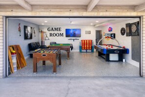A game room with foosball tables, pool tables, and darts.