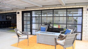 Une terrasse extérieure aménagée avec des meubles en osier, un foyer intégré et une vue dégagée grâce à de grandes portes vitrées.