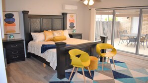 Une chambre à coucher comprenant un lit, des tables de chevet, une chaise, un tapis et une porte-fenêtre coulissante donnant sur un patio.