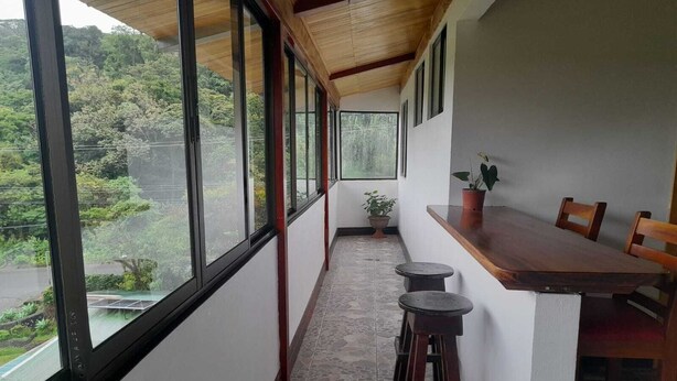 Un balcon étroit avec une table et des tabourets en bois, de grandes fenêtres et une plante en pot.