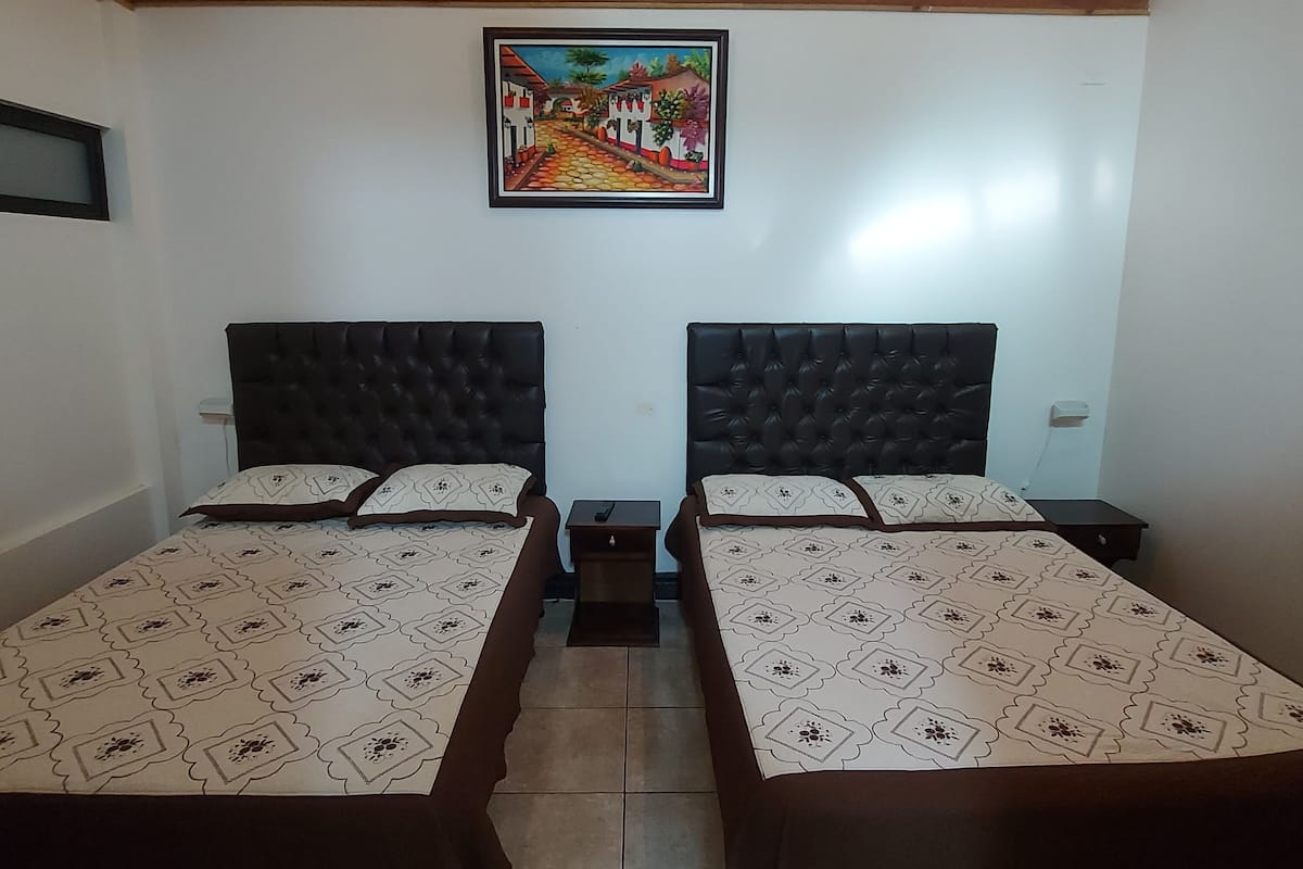 A room with two beds, each with a headboard and a patterned bedspread. There is a painting on the wall above the beds.