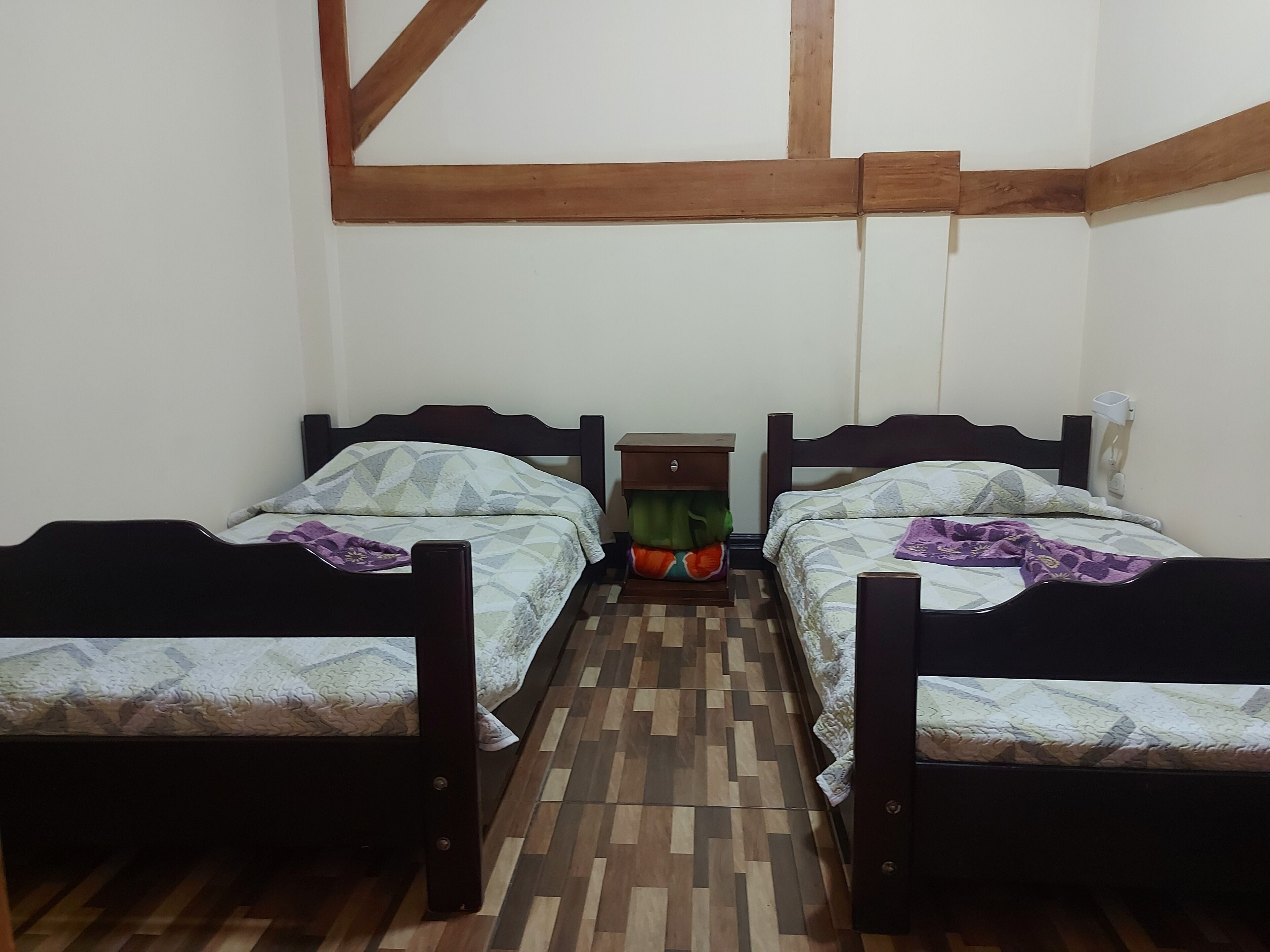 Une petite pièce avec deux lits en bois, une table de chevet et une étagère fixée au mur.