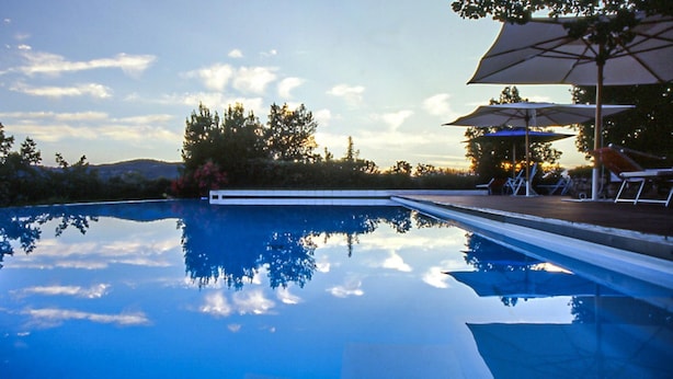 A clear swimming pool with a view of trees and hills in the background.