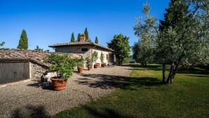 A stone building with a tiled roof, surrounded by gravel and grass, with potted plants and a tree.
