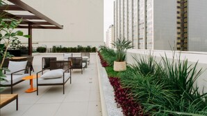 Un patio en la azotea con mobiliario exterior, una pérgola y una hilera de edificios altos al fondo.