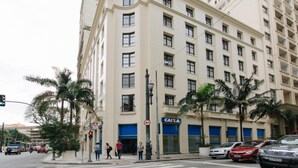 Un edificio de varios pisos con un cartel de 'CAIXA', palmeras y coches estacionados.