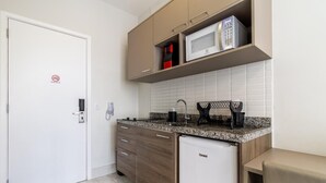 Una cocina compacta con microondas, cafetera y un refrigerador pequeño.