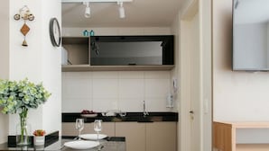 A compact kitchen with a dining area, a yellow stool, and a mounted TV. - Av0111 Studio Avanhandava (São Paulo)