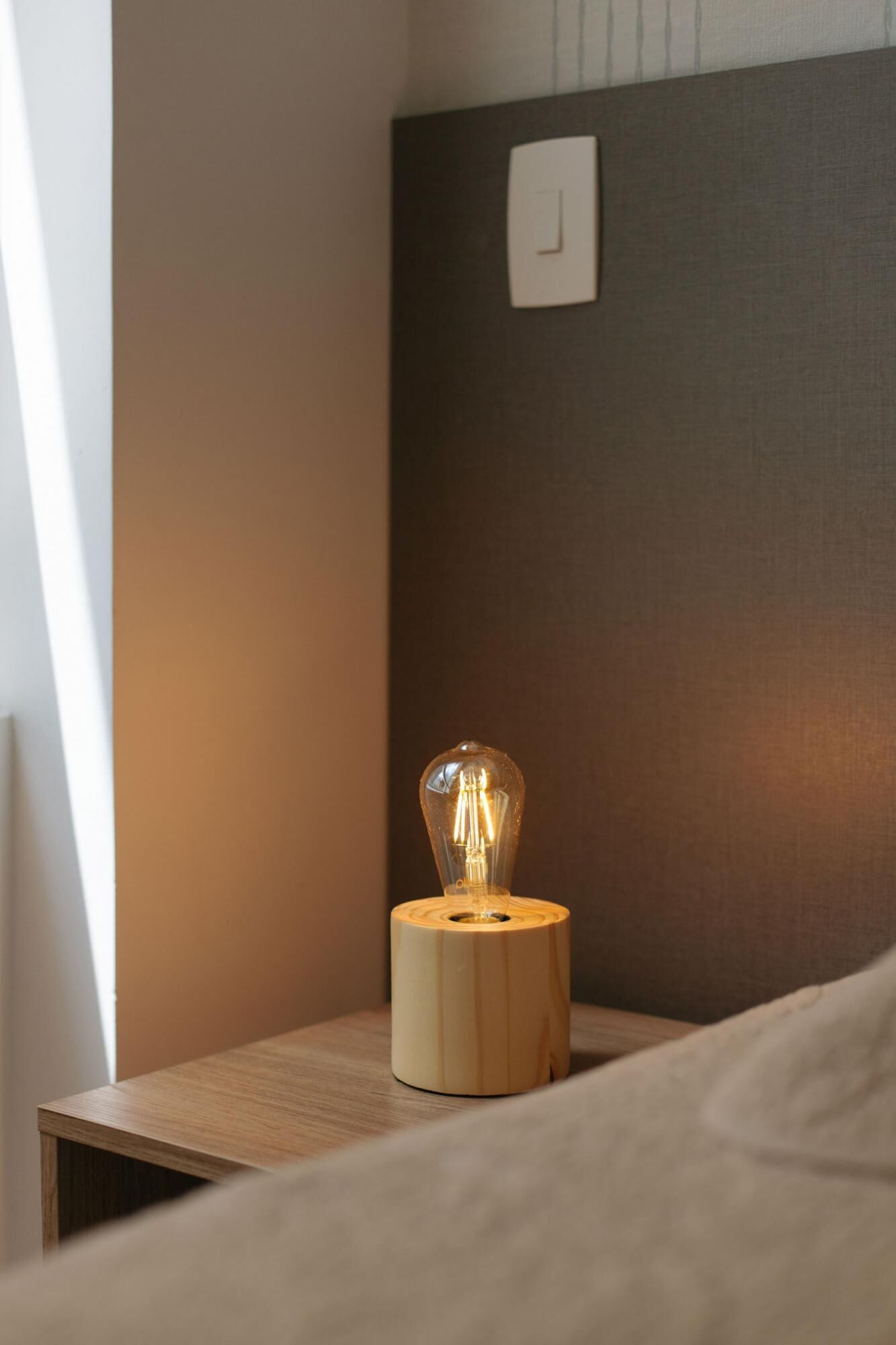 A bedside table with a wooden lamp emitting a warm light.
