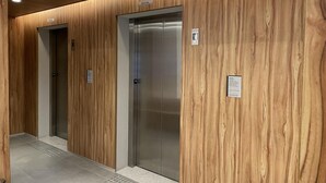 Un couloir doté de deux ascenseurs, de lambris en bois et d’un sol carrelé.