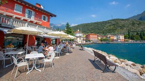 An outdoor café with tables and chairs, a bench, and a view of the sea and mountains. - Residenza al Ponte in Arco (Arco)