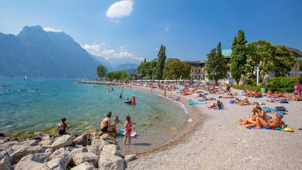 A crowded beach with clear waters, rocky shore, and mountains in the background. - Residenza al Ponte in Arco (Arco)