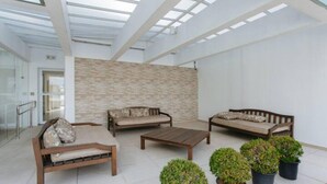 A spacious indoor area with a high ceiling, a stone wall, and multiple seating arrangements including sofas and a coffee table. - Av0408 Studio Avanhandava (São Paulo)