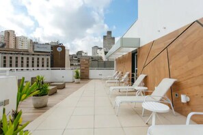 A rooftop terrace with white lounge chairs, potted plants, and a city view. - Av0408 Studio Avanhandava (São Paulo)