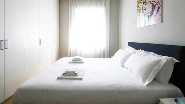 A hotel room with a large bed, white linens, a headboard, and a painting on the wall.