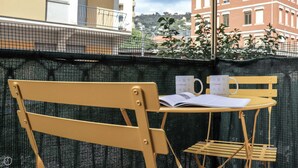 A balcony with a yellow chair and table, two mugs, and an open book.