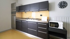 A kitchen with dark cabinets, a gas stove, a microwave, and a wall clock.