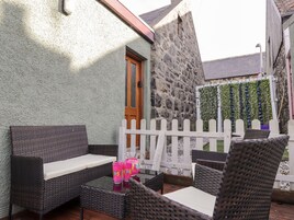 An outdoor seating area with wicker furniture and a table, a stone wall, and a white picket fence.