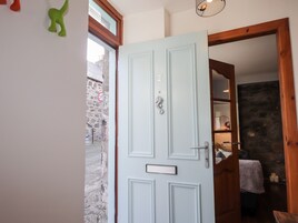A light blue door with a silver handle and a mailbox, leading to a room with a stone wall and a bed with a white blanket.