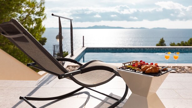 A poolside chair with a grill and drinks, overlooking a pool and mountains.