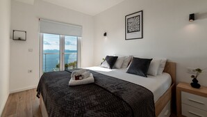 A modern bedroom with a large bed, a view of the sea, and a balcony.