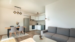 A modern living room with a grey sofa, a white coffee table, and a dining area with a wooden table and grey chairs.